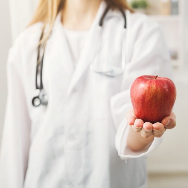 Unrecognizable nutritionist woman with apple sitting at office, copy space. Healthy eating, right nutrition and slimming concept